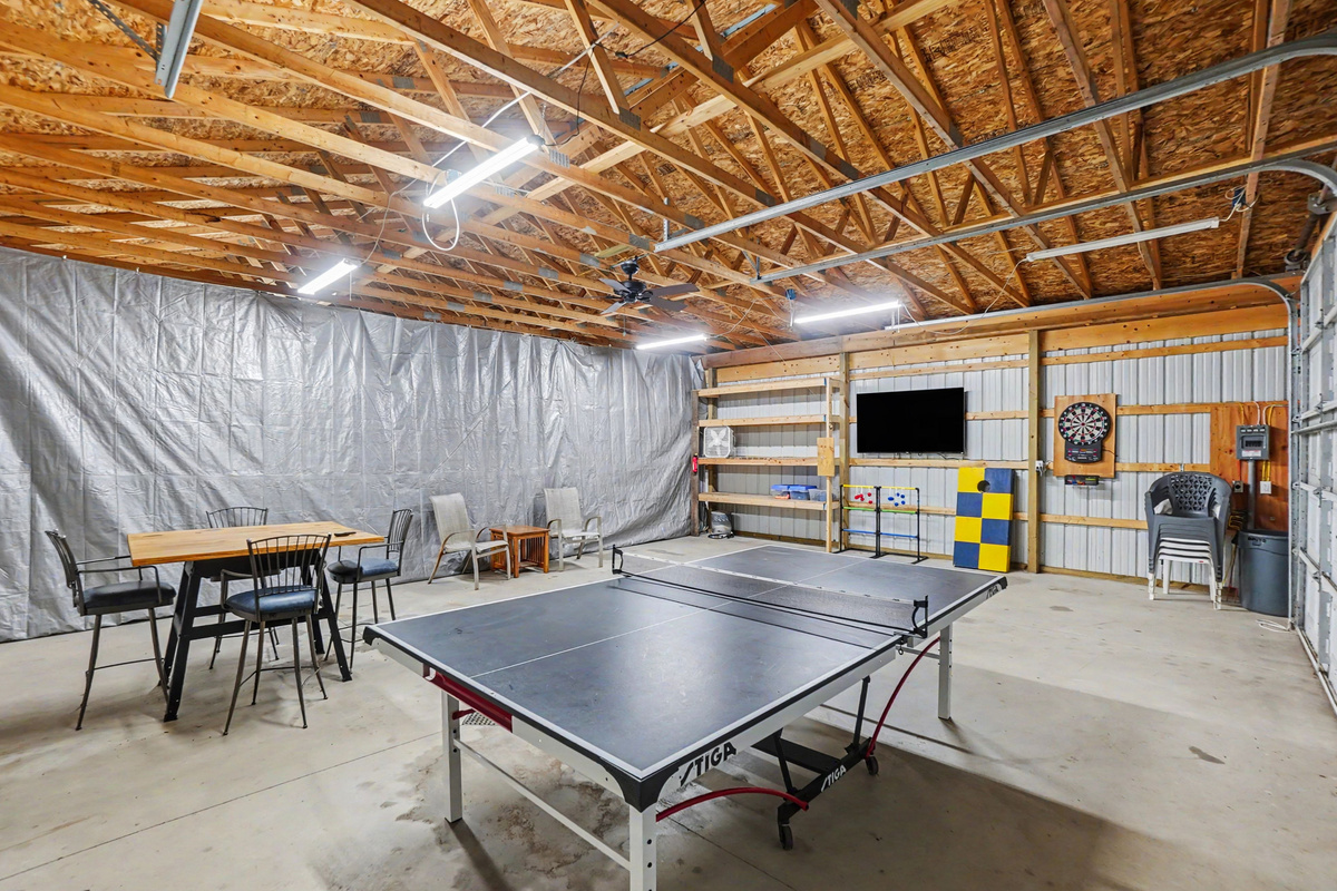 Garage game room with ping pong table, darts, tv and table and chairs.