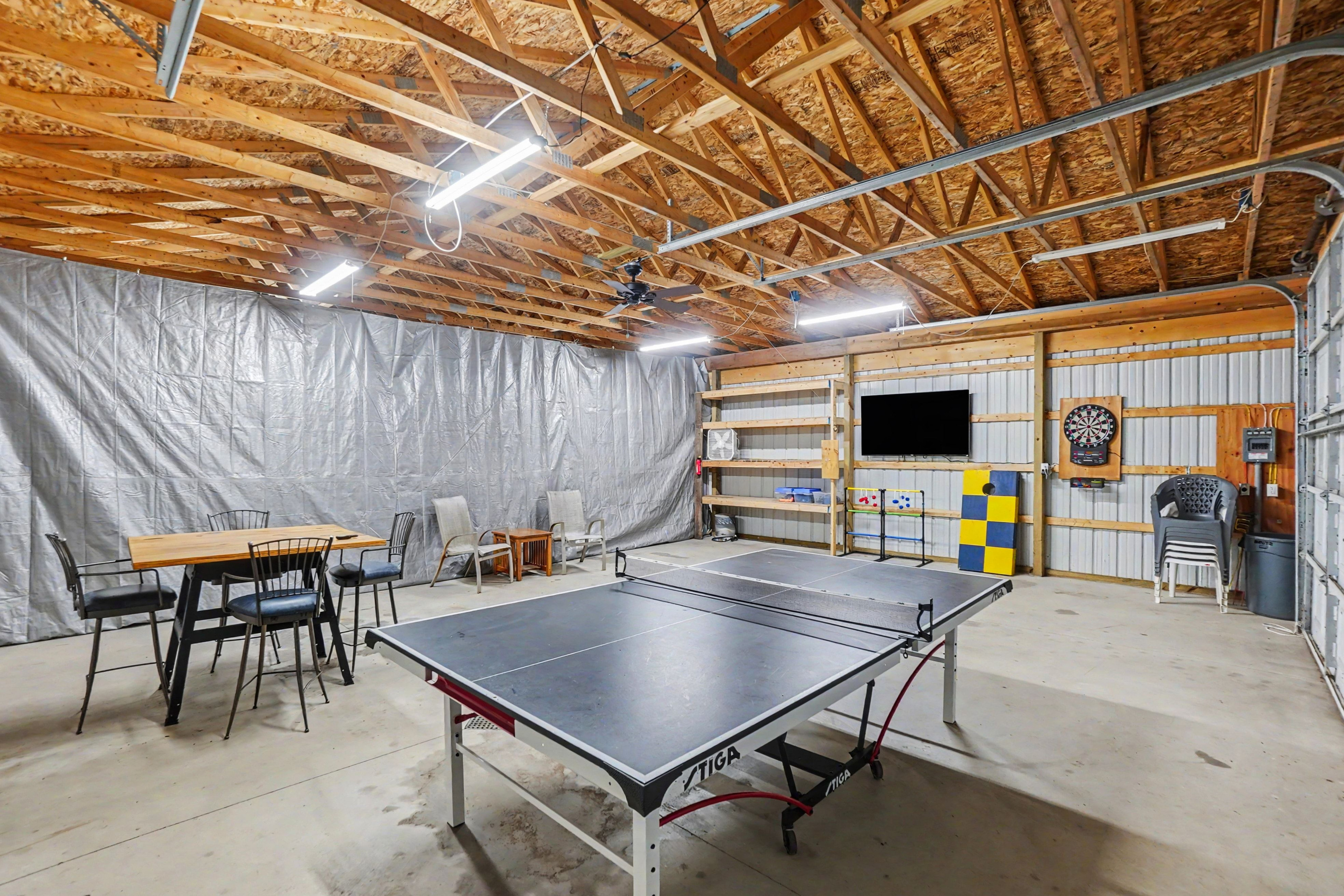 Garage game room with ping pong table, darts, tv and table and chairs.