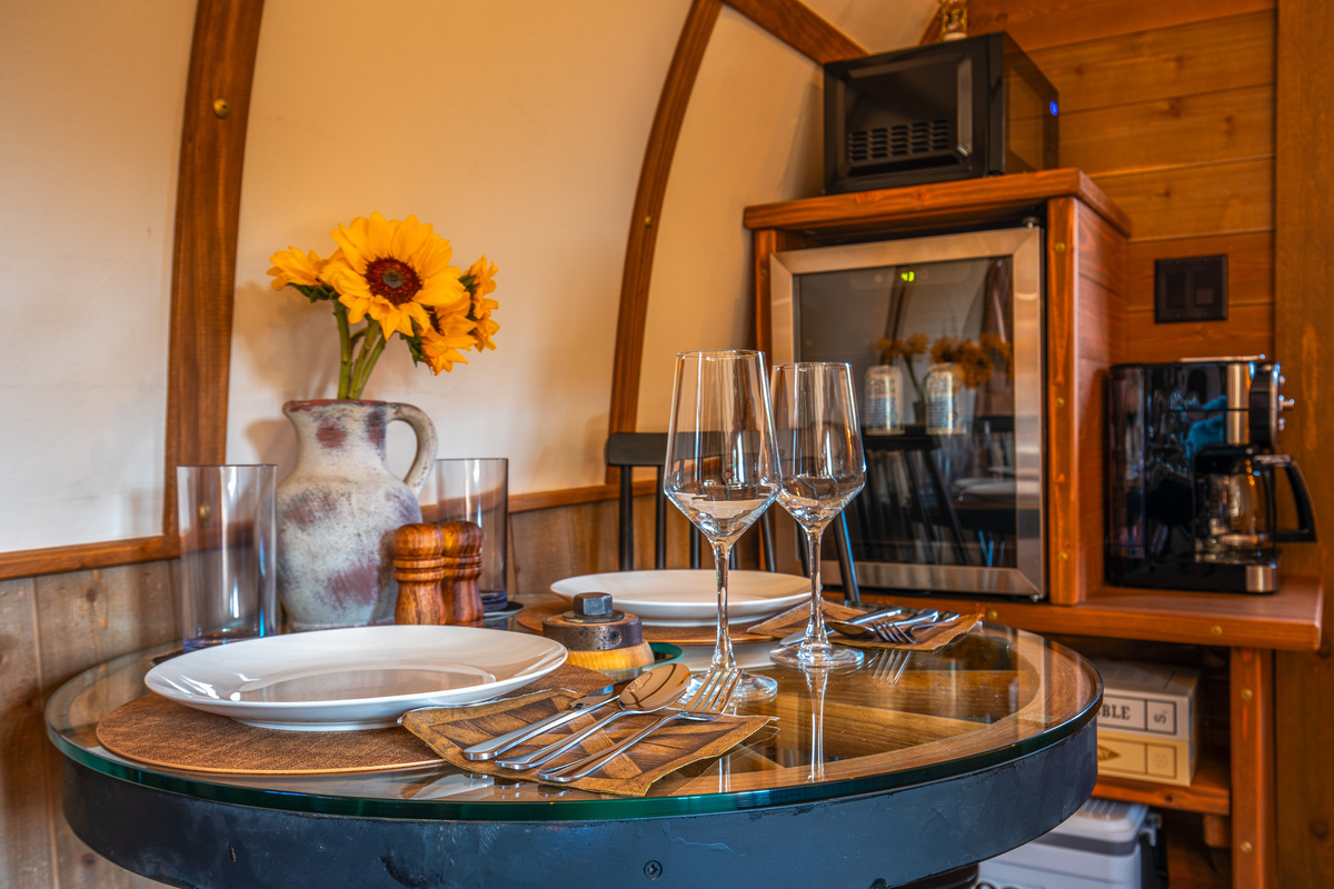Dining setup for two with glassware, coffee station, beverage fridge, and board games nearby.