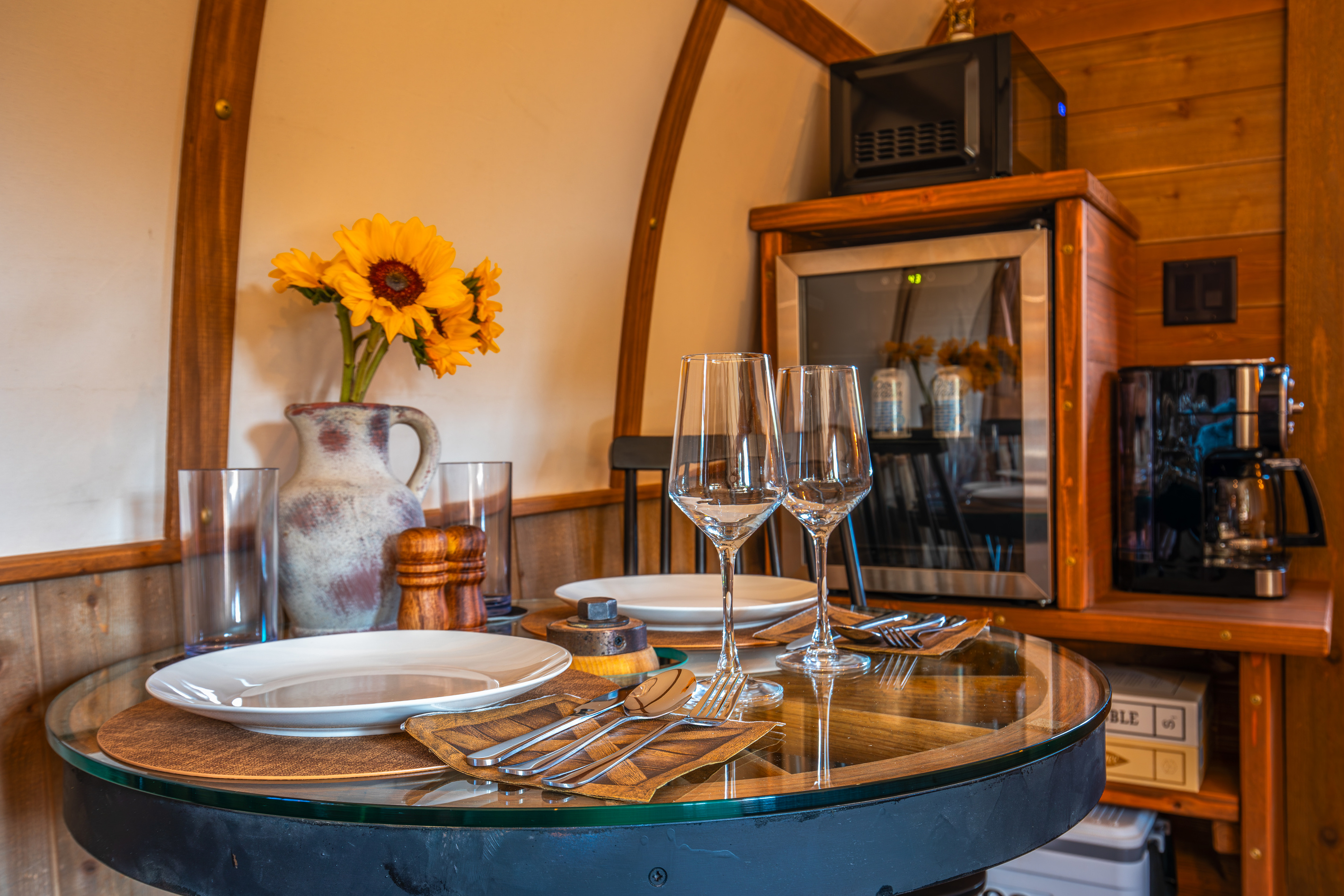 Dining setup for two with glassware, coffee station, beverage fridge, and board games nearby.
