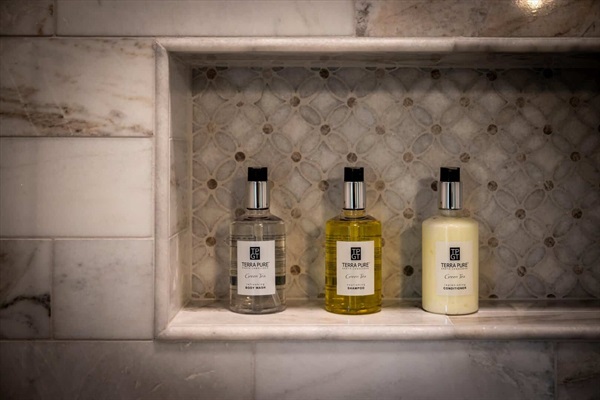Marble shower niche with provided shower gel, shampoo, and conditioner.