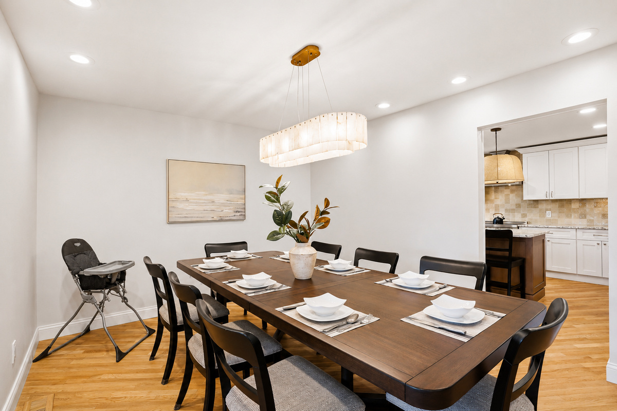 Elegant dining room with a large table, modern seating, and bright chandelier lighting. Clean, stylish space ideal for family meals and entertaining.