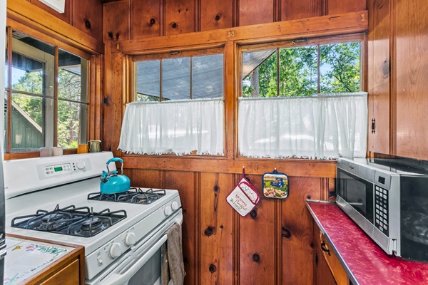 The kitchen features a vintage stove, microwave, and forest views, making cooking a joy during your stay.