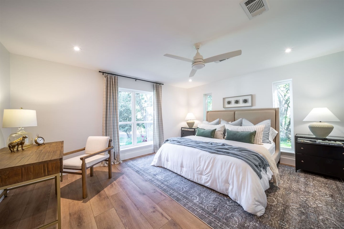 Bedroom 3 features a comfortable bed with layered neutral bedding, a ceiling fan, and abundant natural light. The room includes a dedicated workspace, making it ideal for both relaxation and remote work during longer stays.