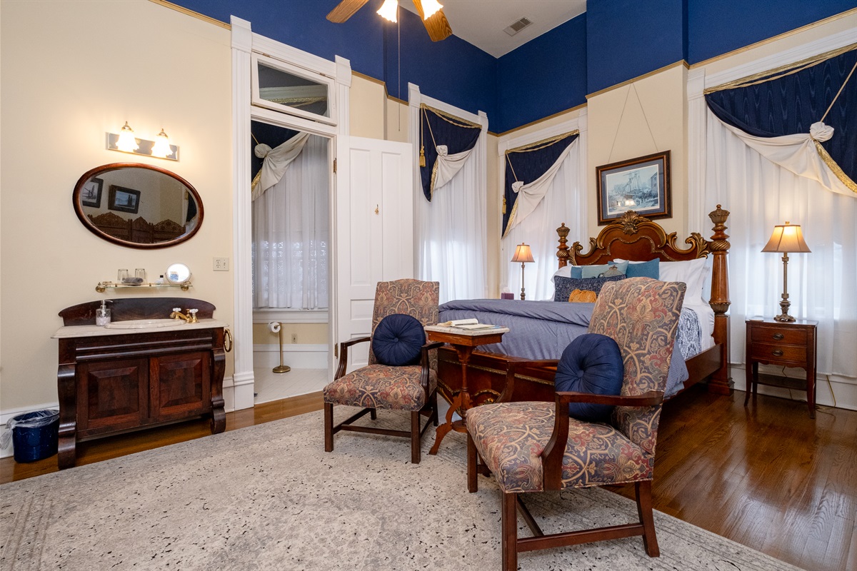 Primary sleeping area with carved wood bed, tall windows, and period-inspired décor.