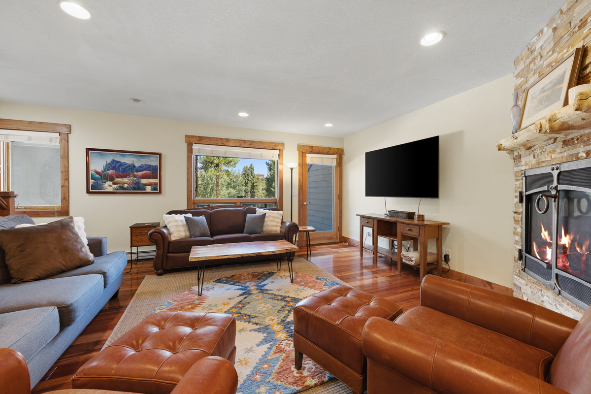 Living room with two sofas, two recliners, large TV, balcony, gas fireplace and brand new large area rugs for on-the-floor playtime in the center of the home. 