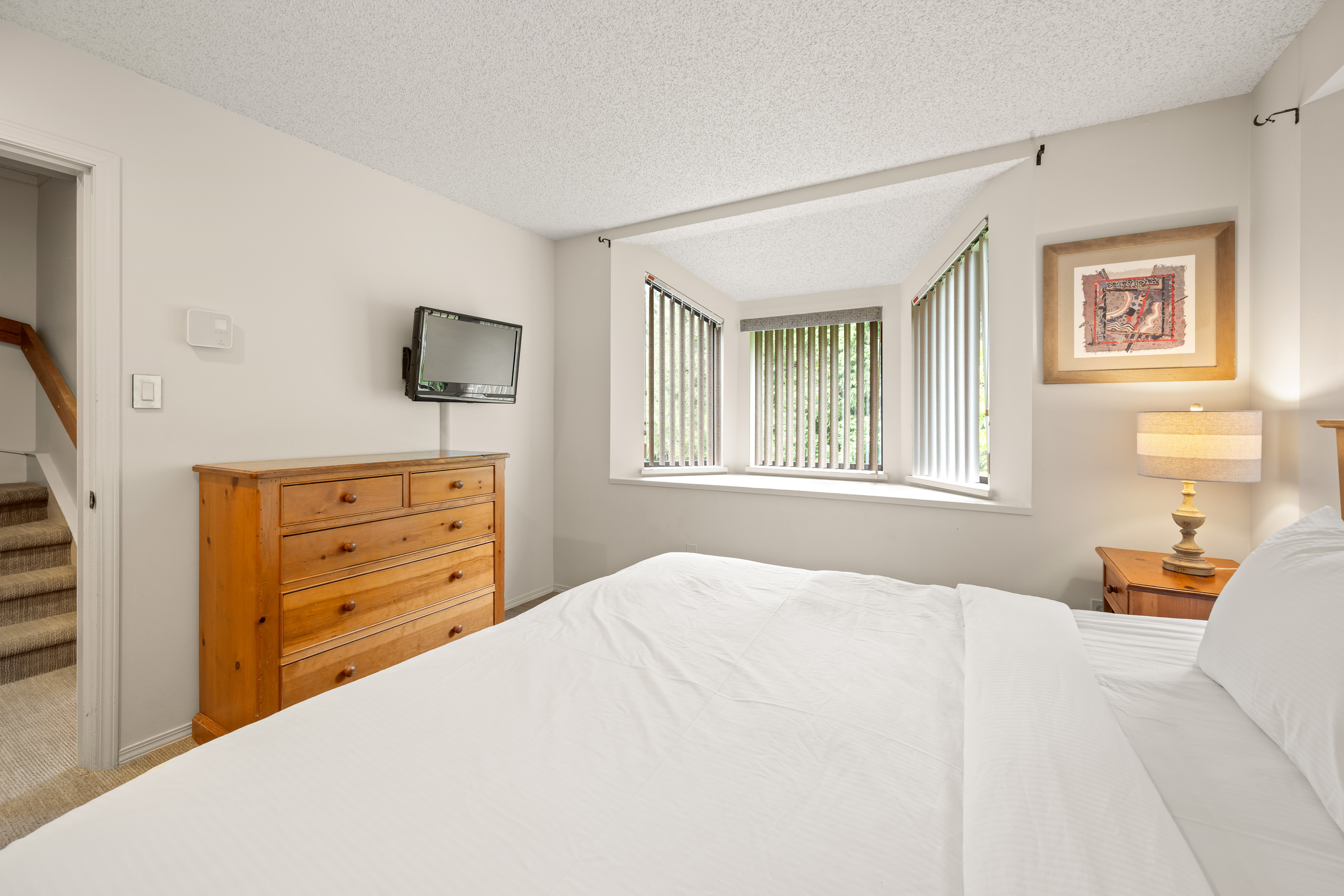 Primary bedroom (queen bed) with a wood dresser, a wall-mounted TV and a bay window on the 2nd floor.