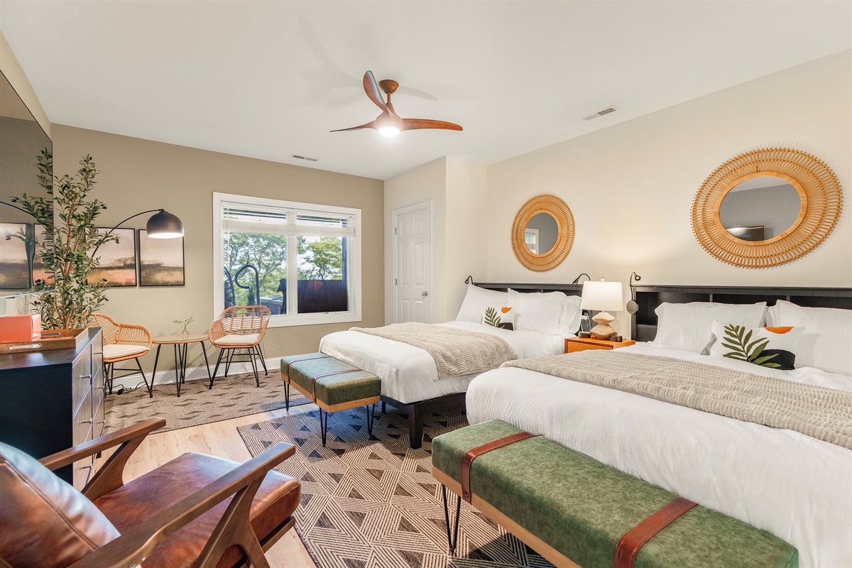 Spacious and stylish, this double-queen suite blends mid-century charm with modern comfort—featuring a 75" TV, ceiling fan, and serene window views of the patio and treetops beyond