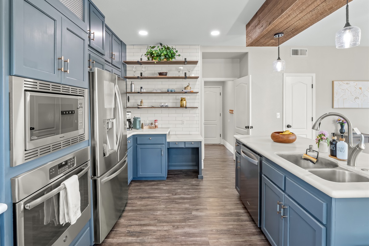 Designer kitchen featuring custom blue cabinetry, quartz countertops, stainless steel appliances, statement wood beam, and open shelving—an elevated space made for gathering, cooking, and entertaining in style.