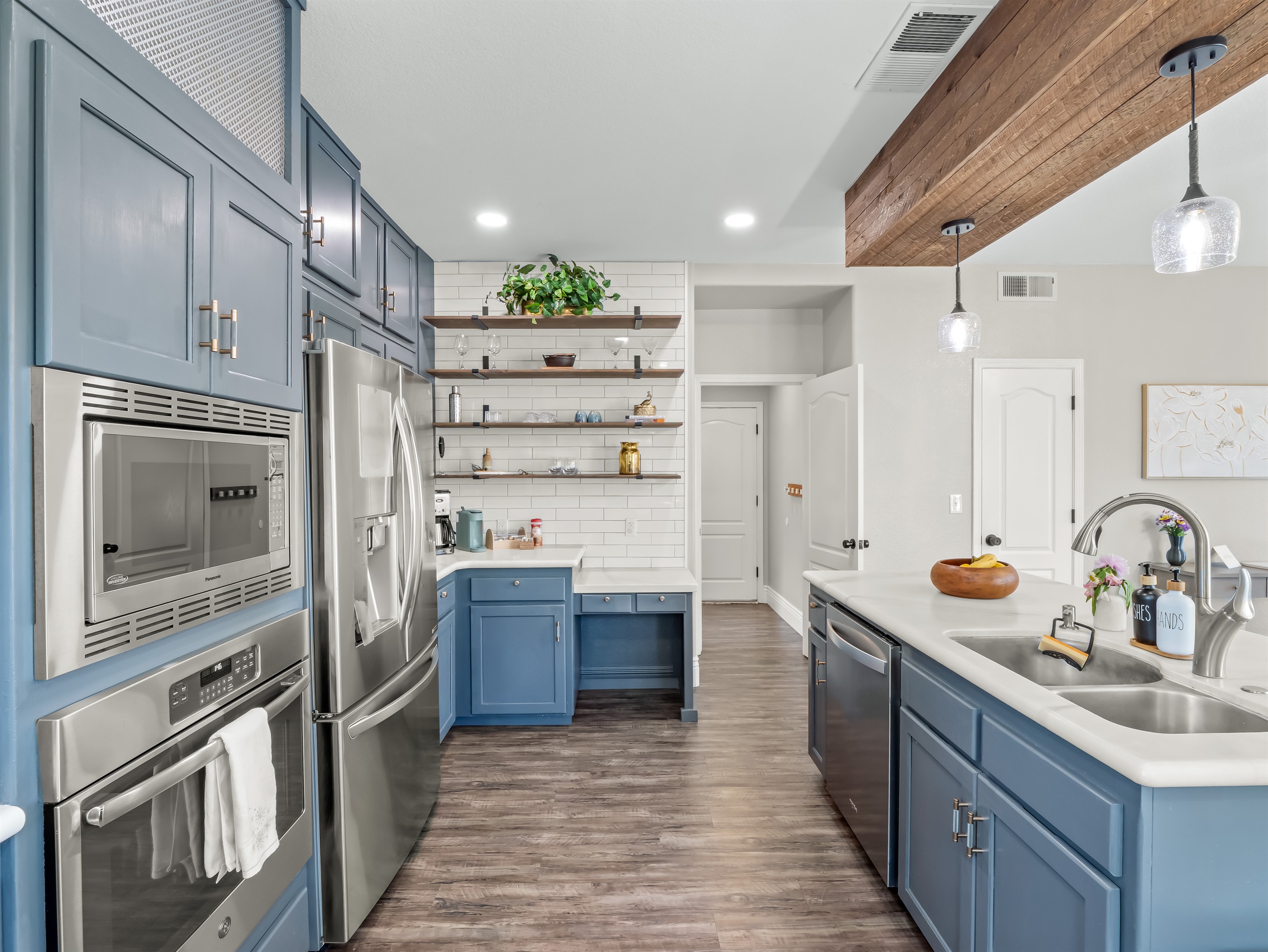 Designer kitchen featuring custom blue cabinetry, quartz countertops, stainless steel appliances, statement wood beam, and open shelving—an elevated space made for gathering, cooking, and entertaining in style.
