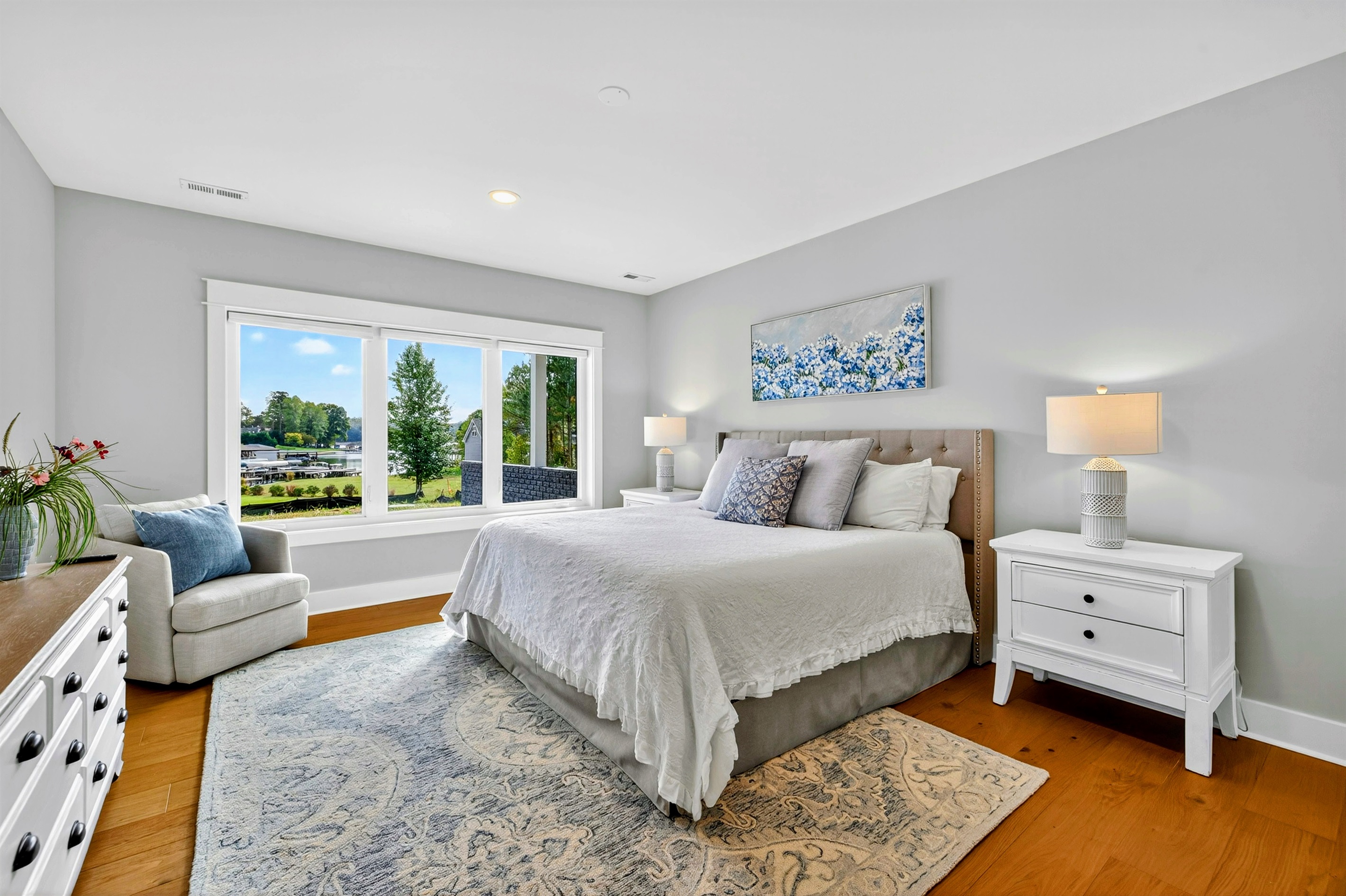 The king "Hydrangea Room" is finished in soft grays, whites, & blues, featuring luxury bedding, a plush white comforter, and a feathery soft bed. Expansive windows offer stunning lake views. Every detail is curated to offer guest that retreat feel!