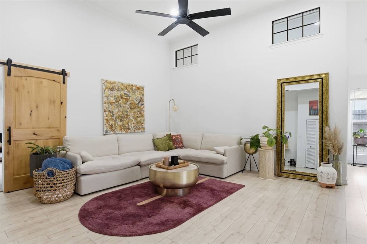 Bright open-concept living room with sectional sofa, Smart TV with streaming, ceiling fan, high ceilings, fast WiFi, and stylish seating perfect for relaxing or movie nights.