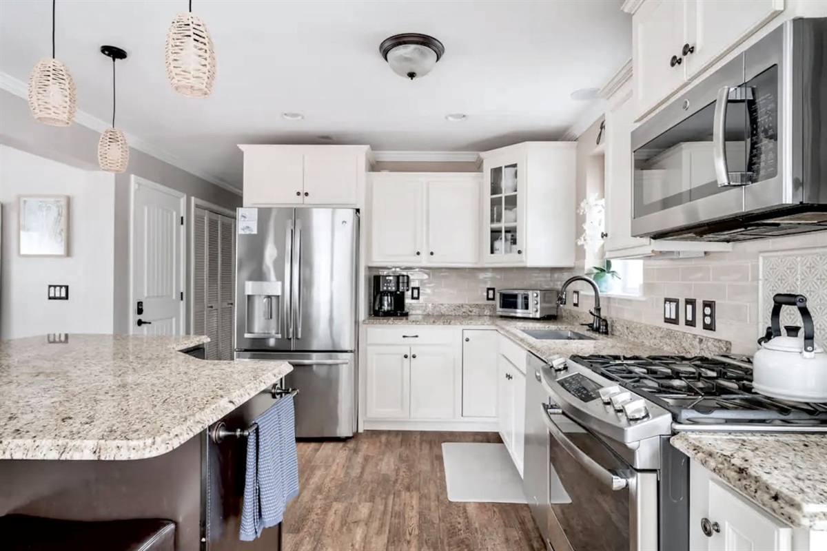 Cook with ease in this bright, modern kitchen featuring stainless steel appliances, granite countertops, and an island. White cabinetry and stylish pendant lighting create a clean, inviting space perfect for preparing any meal.