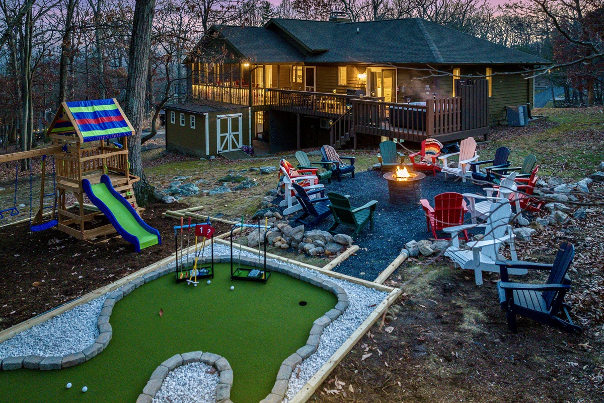 view of the back yard with the firepit with plenty of chairs, mini golf, playset and you can see the house behind with the private hot tub