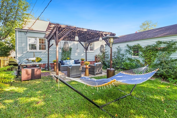 Unwind beneath the pergola—our South Bend guest retreat features a cushioned sofa, hammock, patio heater, and grill station. Cozy alfresco vibes and flavorful moments near Notre Dame.