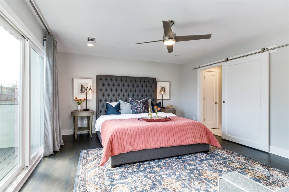 - Comfortable bed with tufted headboard, vibrant coral bedding, and designer pillows - Sliding barn door leads to a private bath, adding farmhouse style charm - Large rug, curated artwork, and soft lighting create a stylish yet cozy retreat