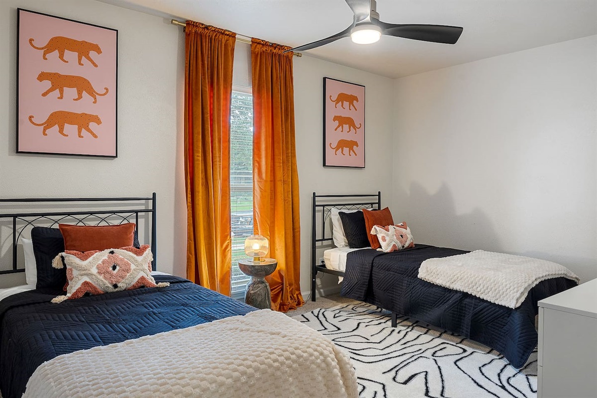 This bedroom is designed for comfort with two twin beds, vibrant artwork, and ample natural light. The ceiling fan ensures a pleasant stay.