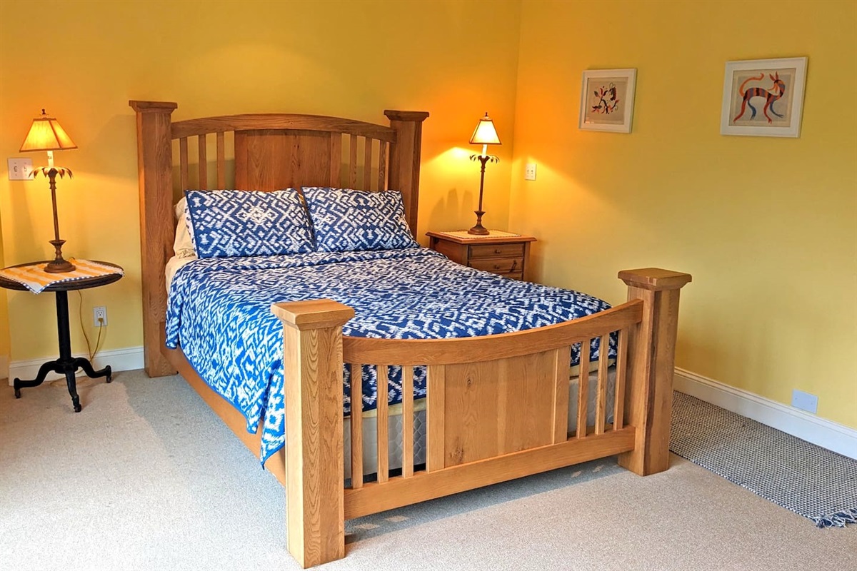 - Cozy bedroom with wooden bed frame, blue patterned bedding, and warm lighting  
- Soft yellow walls add brightness and a cheerful touch to the space  
- Includes nightstands with lamps for evening reading or ambiance