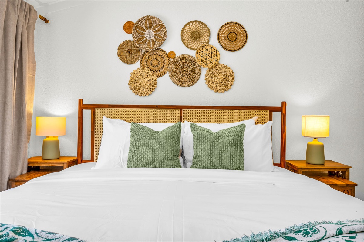 Serene ensuite primary king suite featuring a plush bed with luxury linens, vaulted ceilings with exposed beams, and elegant coastal décor. Includes a spacious walk-in closet with washer and dryer for added convenience and comfort.