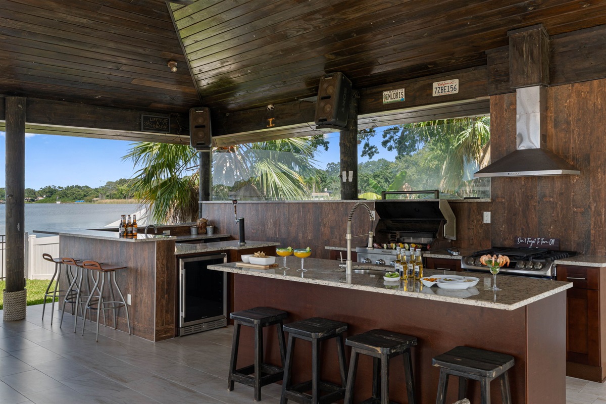 This expansive covered patio offers a full kitchen, bar seating, hanging chairs, and lounge areas, all with stunning waterfront views.