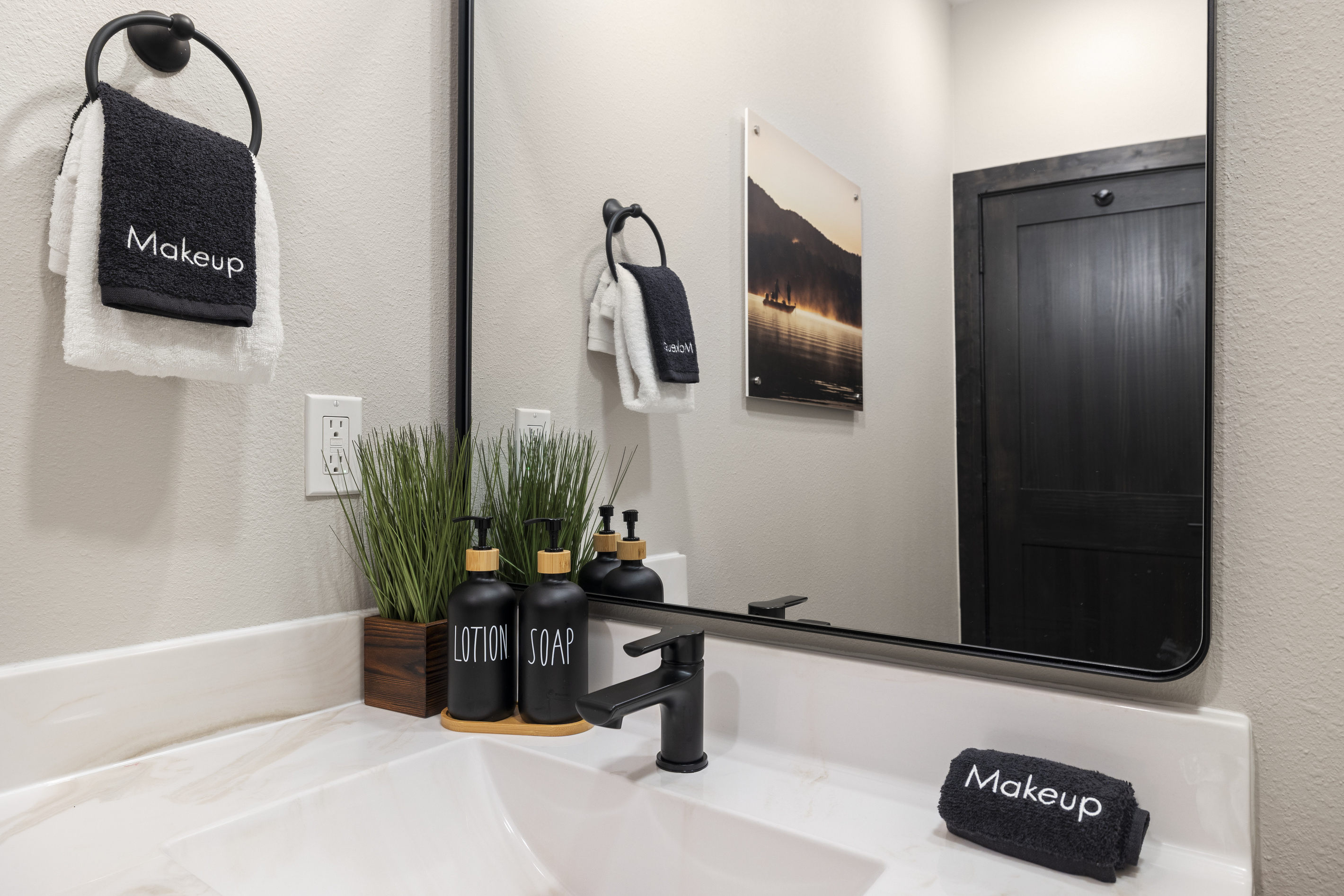 Lake-at-dawn art hangs over a black-fixture vanity.