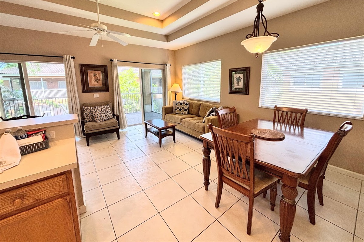 Open and inviting dining and living space with tile flooring, tray ceilings, plenty of natural light, and sliding glass doors opening to a private balcony.