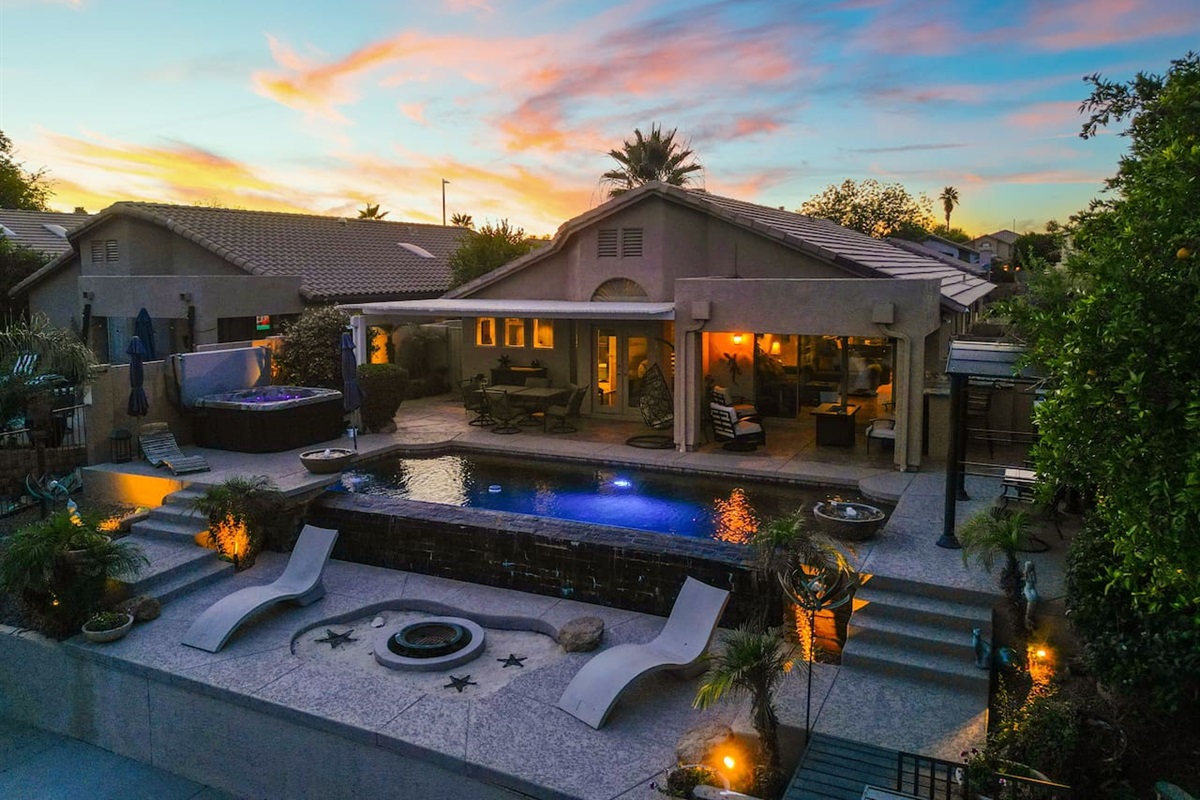 An aerial view at golden hour reveals the full picture — sparkling pool, bubbling hot tub, fire pit terrace, and a warmly lit covered patio, all coming together for the ultimate Arizona backyard experience.