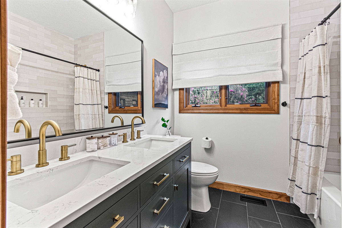 This beautifully updated bathroom features a dual vanity, gold accents, and a tub shower, near the Biltmore and Laurel Falls Bedrooms.🛁✨