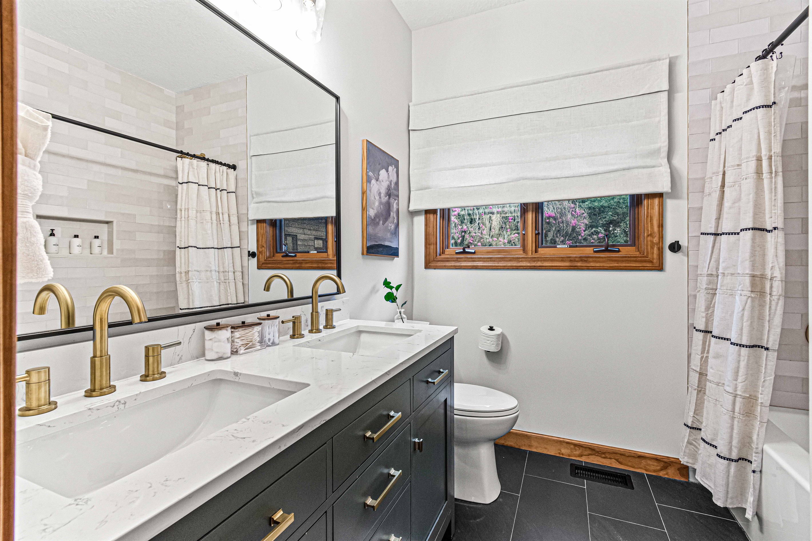 This beautifully updated bathroom features a dual vanity, gold accents, and a tub shower, near the Biltmore and Laurel Falls Bedrooms.🛁✨