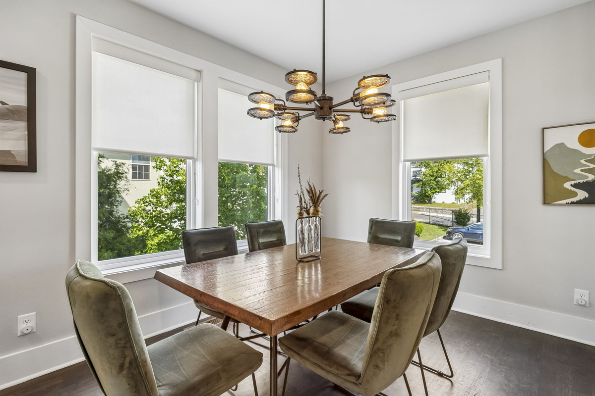 Light filled corner dining room with large windows and sleek contemporary layout - Olive green velvet chairs surround a warm wood table under a sculptural light fixture - Perfect for meals, board games, or casual coffee with natural sunlight all day
