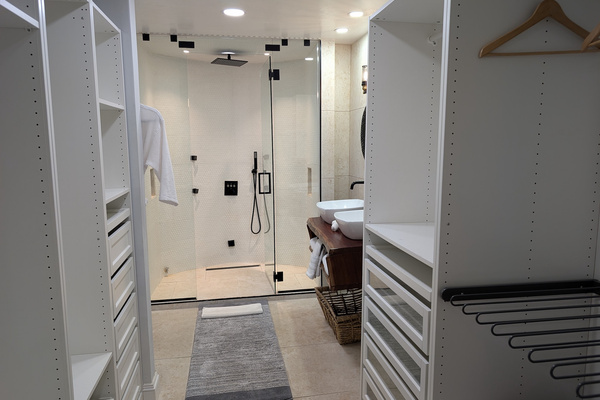 Primary bedroom ensuite bathroom at Villa Coral featuring a large walk-in closet organization system, a dual-sink vanity, and a glass-enclosed rainfall shower in Dorado, Puerto Rico.
