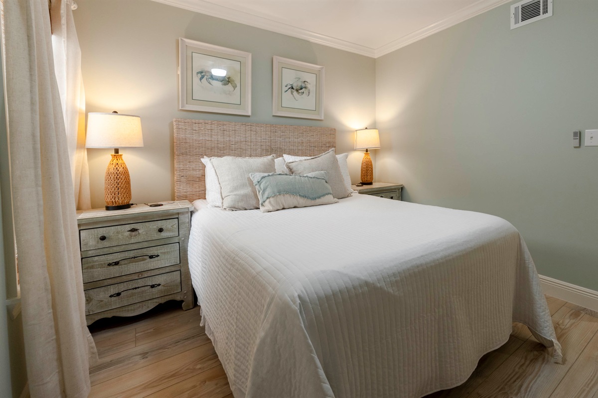 Unwind in a serene bedroom at “Gone Coastal” in Gulf Shores, AL, with a wicker headboard, queen bed, soft lighting, and elegant decor.
