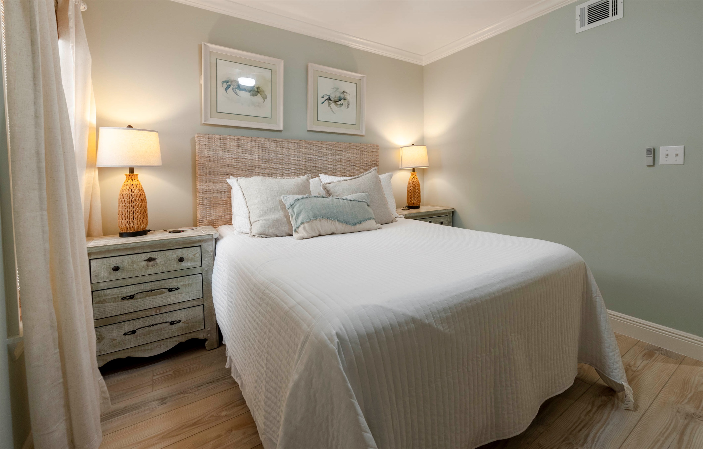 Unwind in a serene bedroom at “Gone Coastal” in Gulf Shores, AL, with a wicker headboard, queen bed, soft lighting, and elegant decor.
