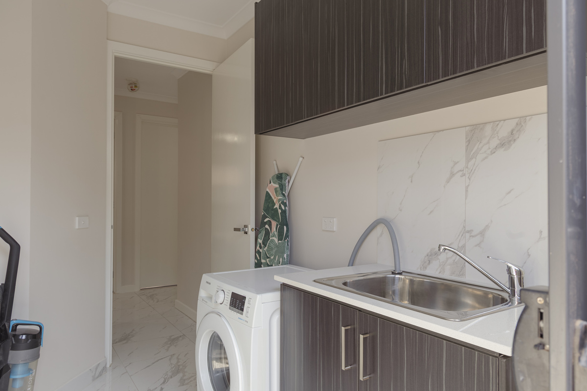 This laundry includes a washing machine, utility sink, overhead cupboards and an ironing board, helping longer stays feel simple and organised