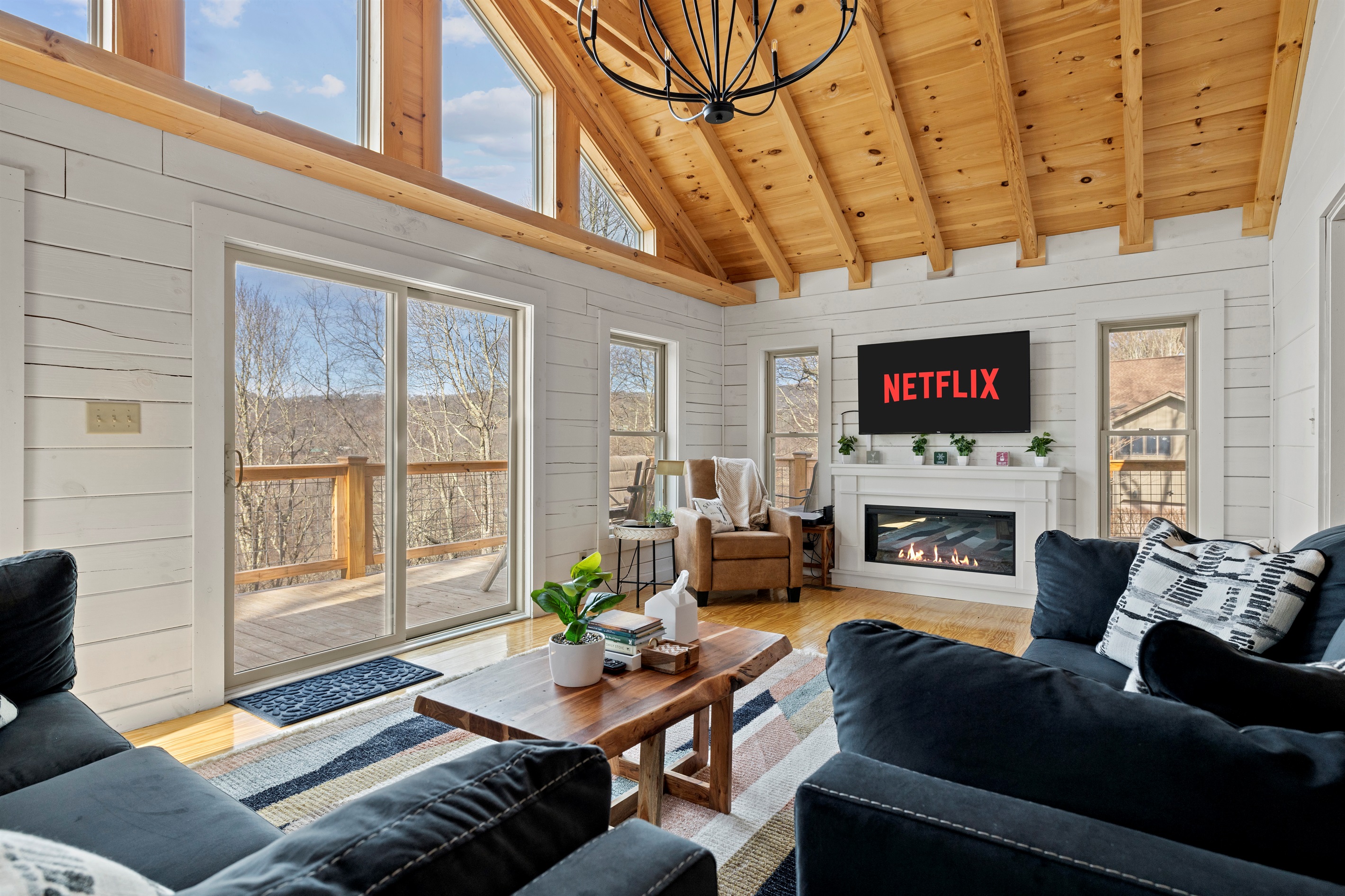 A cozy yet grand family room framed by floor-to-ceiling mountain views, where a glowing fireplace and beautifully decorated!