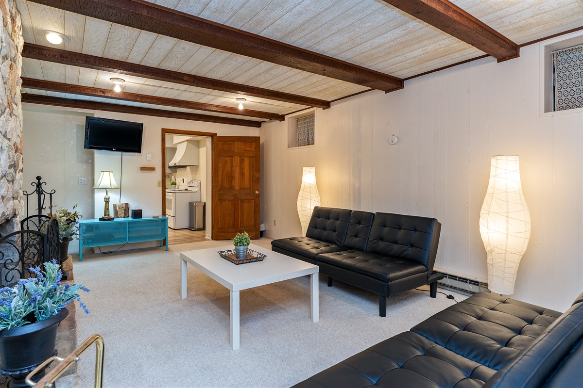 Unwind in the inviting basement level living room with plush seating and a stunning stone fireplace – a perfect spot for cozy evenings.