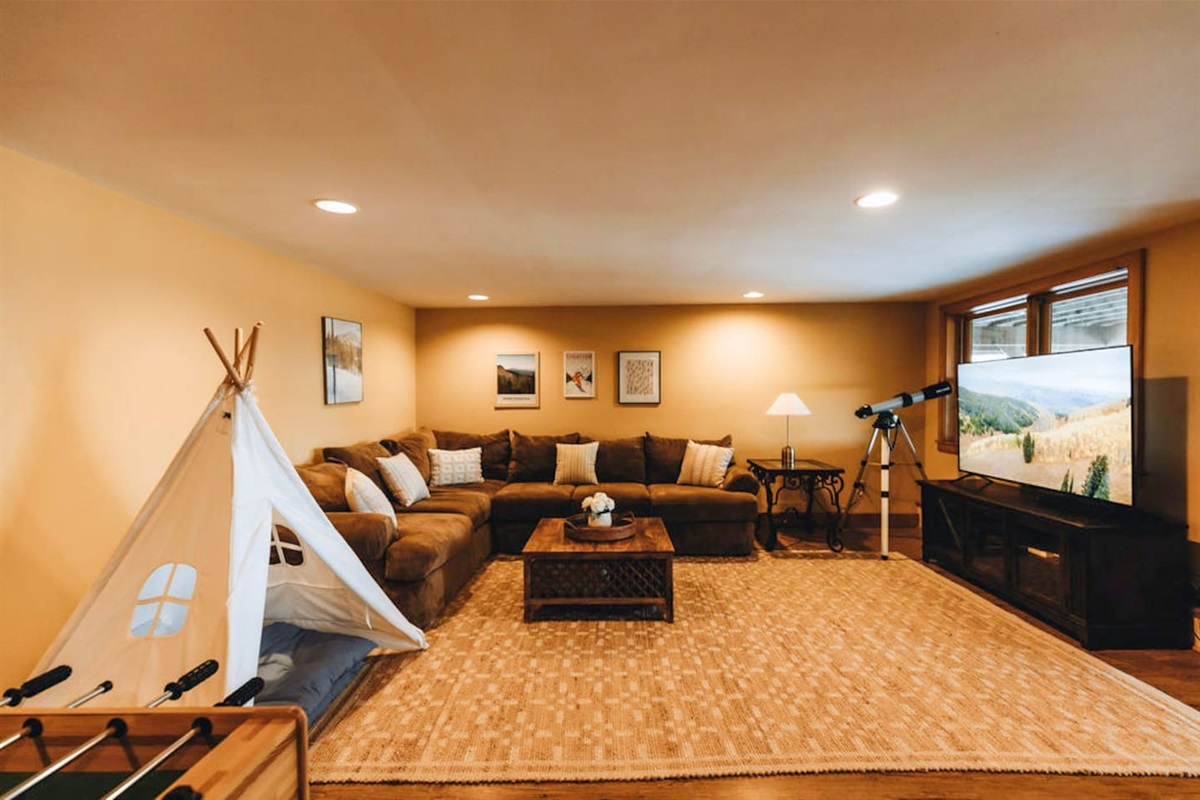 The lower level family room / game room features a large sectional sofa, football table, pingpong table, a 65" TV, a telescope for star gazing... and even a teepee for the kiddos