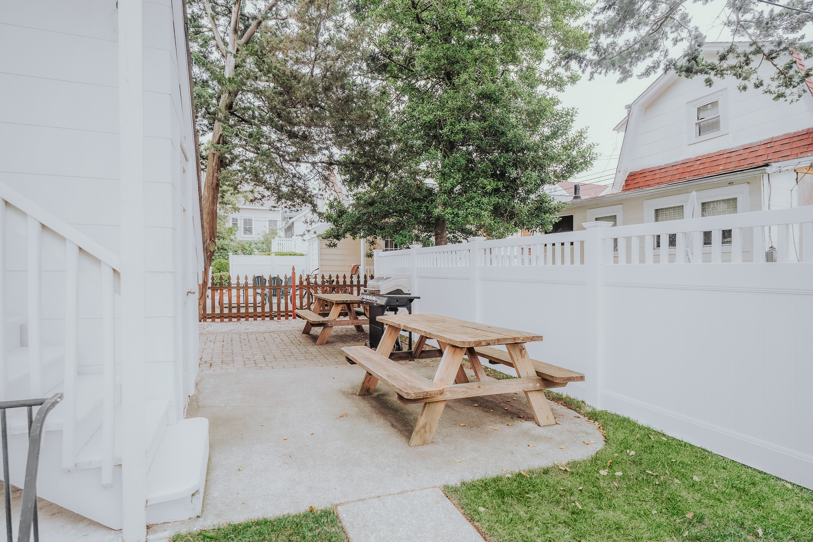 Side Patio Area Featuring Wooden Picnic Tables, Lawn Strip, and Privacy Fence