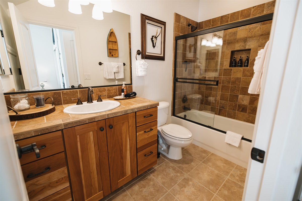 Warm, lodge-style bathroom with full vanity, glass-enclosed tub/shower, plush towels, and stocked essentials—perfect for refreshing after hiking, skiing, or a cozy night in.