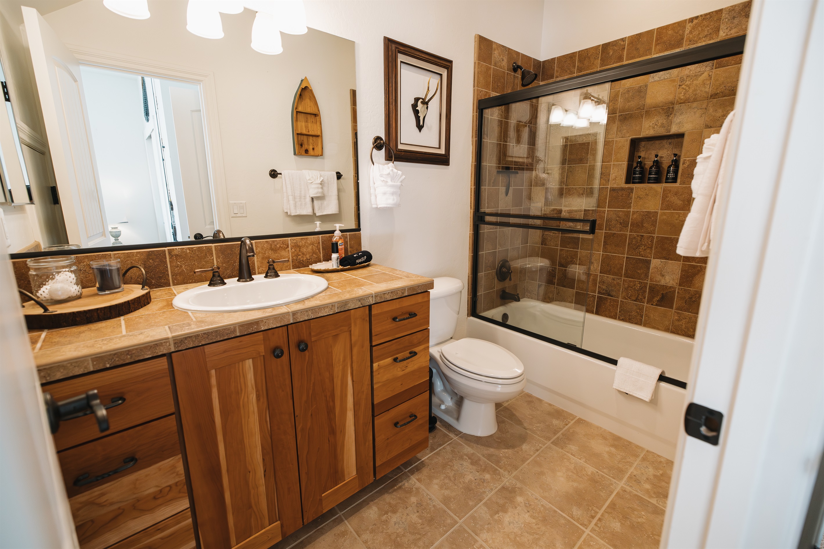 Warm, lodge-style bathroom with full vanity, glass-enclosed tub/shower, plush towels, and stocked essentials—perfect for refreshing after hiking, skiing, or a cozy night in.