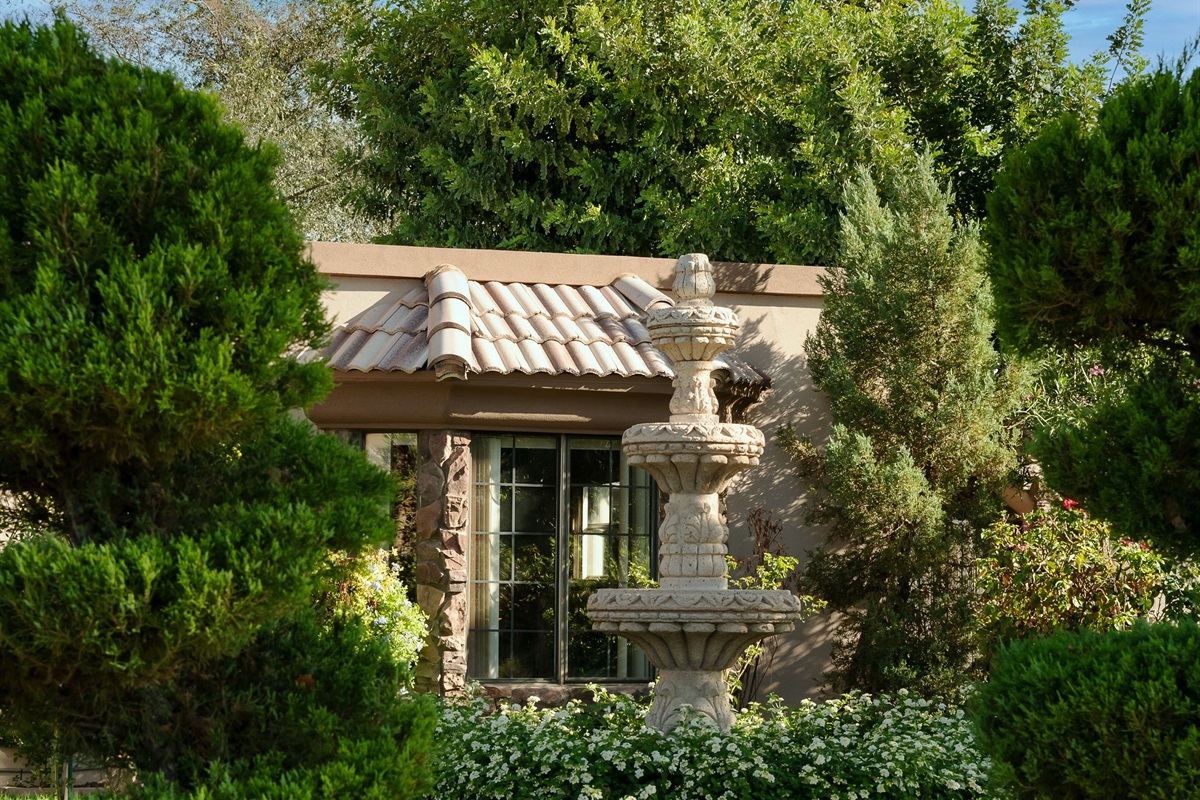 Unwind in this tranquil garden hideaway, where rich greenery and a charming stucco structure create a secluded outdoor sanctuary.