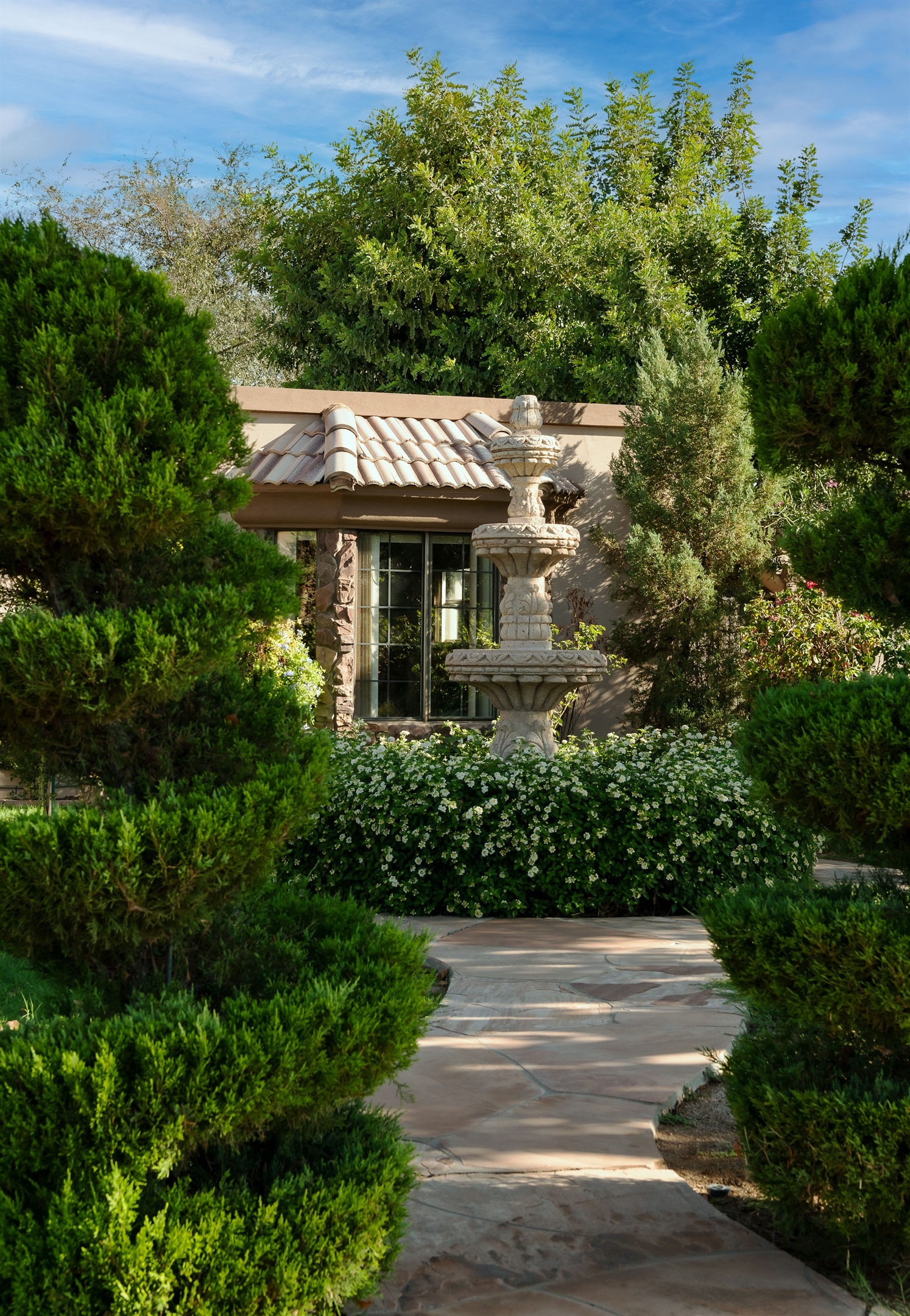 Unwind in this tranquil garden hideaway, where rich greenery and a charming stucco structure create a secluded outdoor sanctuary.