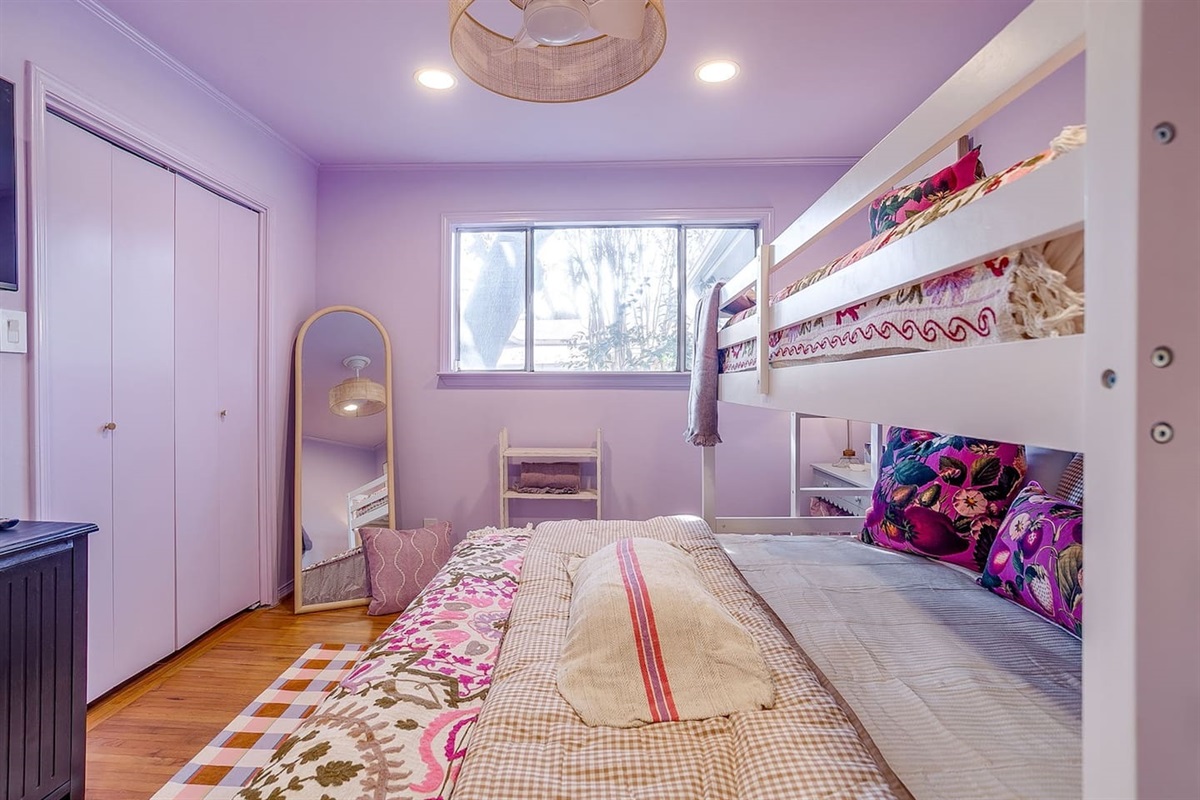 Bedroom Three from another angle — full-size mirror for outfit checks, natural light through the window, ample closet space, and a king bunk layered in crisp bedding.