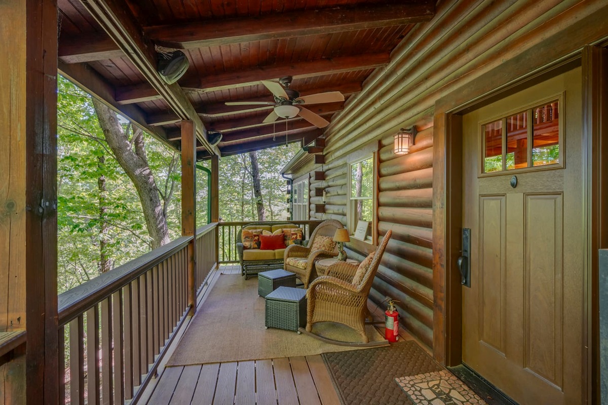 Welcoming front entrance with a covered wraparound porch, comfortable seating, and peaceful wooded views
