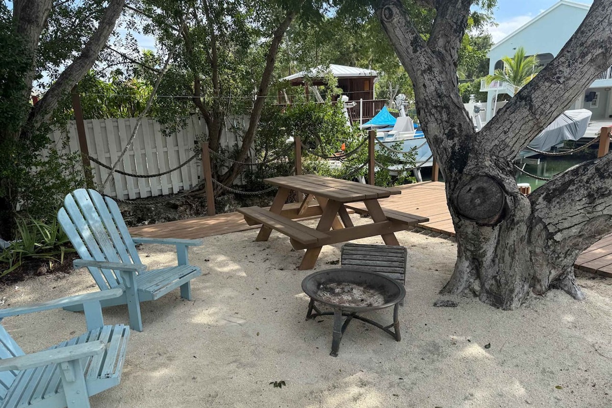 Sandy and shady area with chairs, picnic table and fire pit