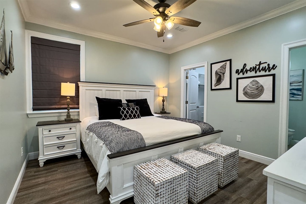 A calm, coastal-inspired bedroom with a crisp white bed frame, soft gray tones, warm lighting, and the convenience of a private ensuite bath just steps away.