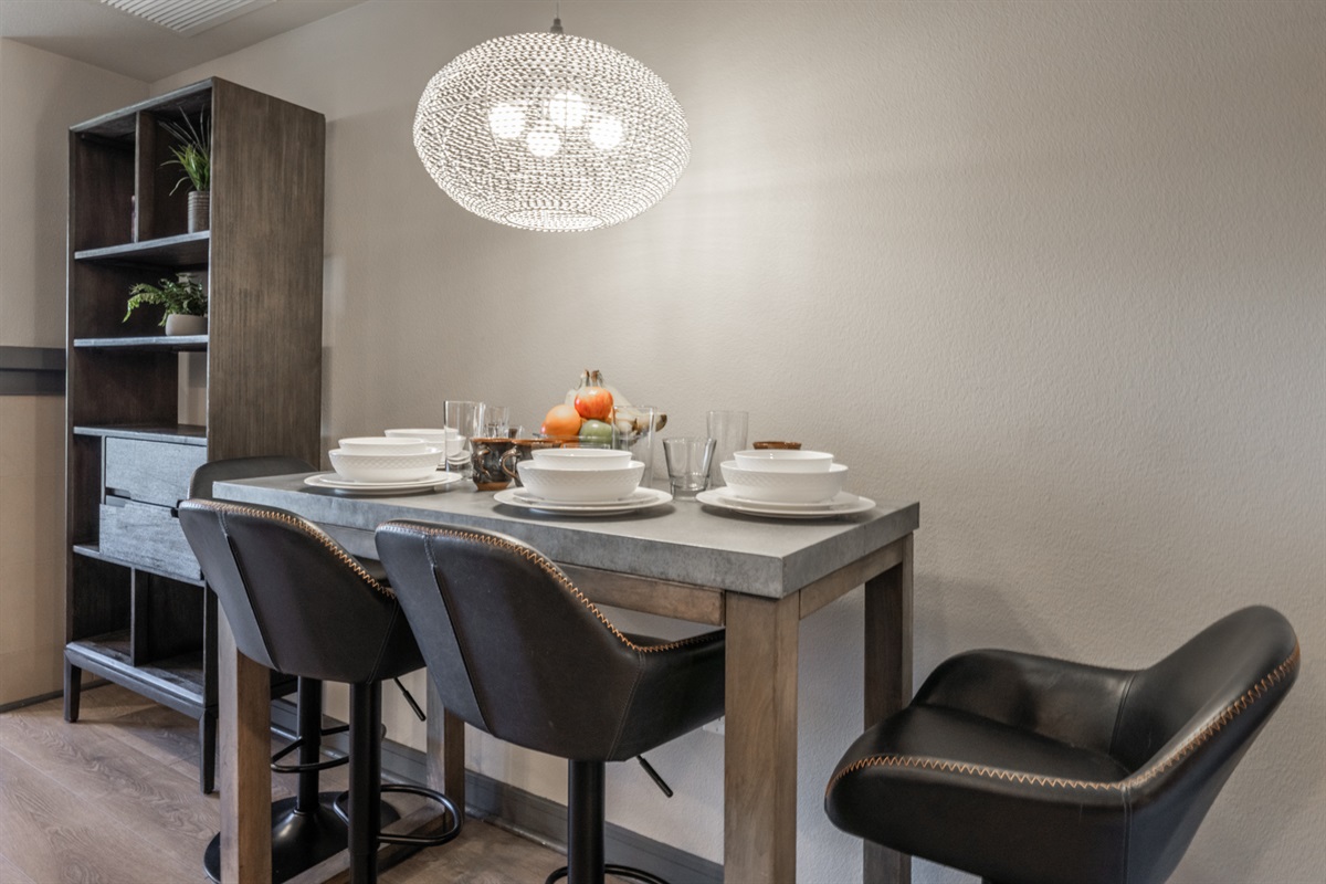 A modern bar-height table with leather stools seats four comfortably, ideal for meals, work, games, or planning the day.