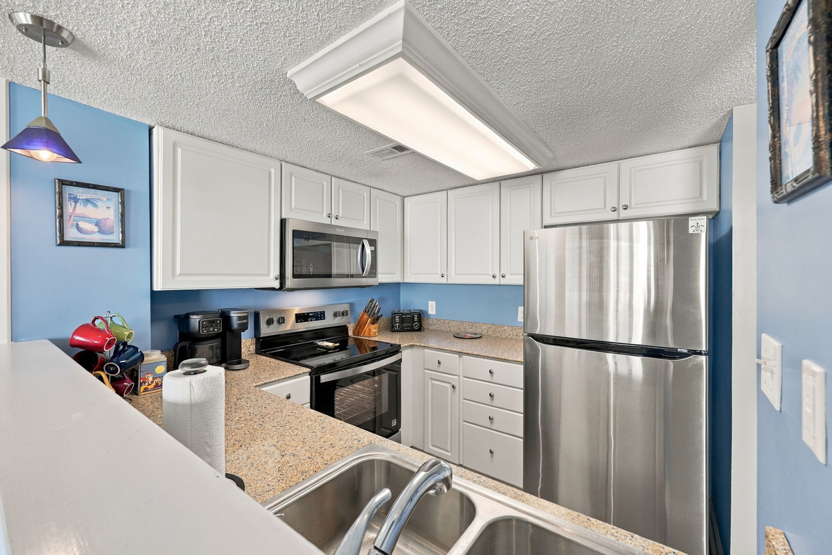 Fully equipped kitchen with white cabinetry, stainless steel appliances, double-basin sink, and blue accent walls.