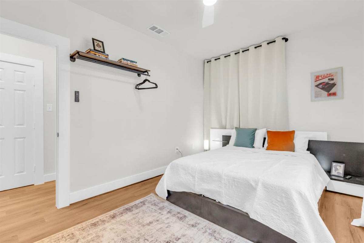 Main bedroom with queen bed, room darkening shades, hangars, and modern decor.