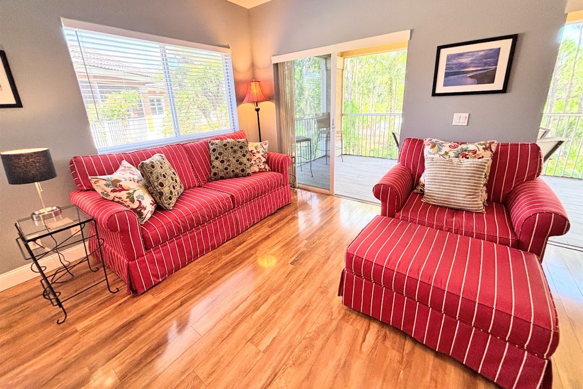 Comfortable living area featuring cozy red seating, wood-look flooring, and large windows overlooking the greenery.